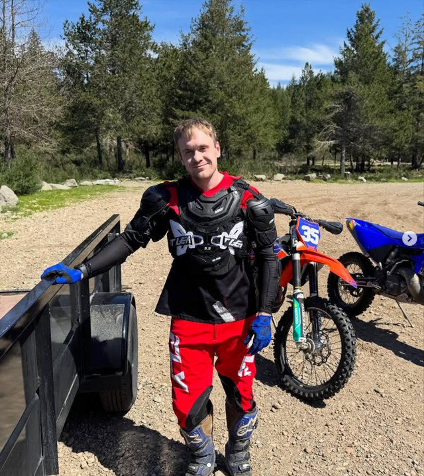 Alexander Pennington in motocross gear, leaning on a trailer next to his orange dirt bike in the woods